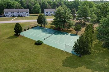 A tennis court is surrounded by trees and houses.
